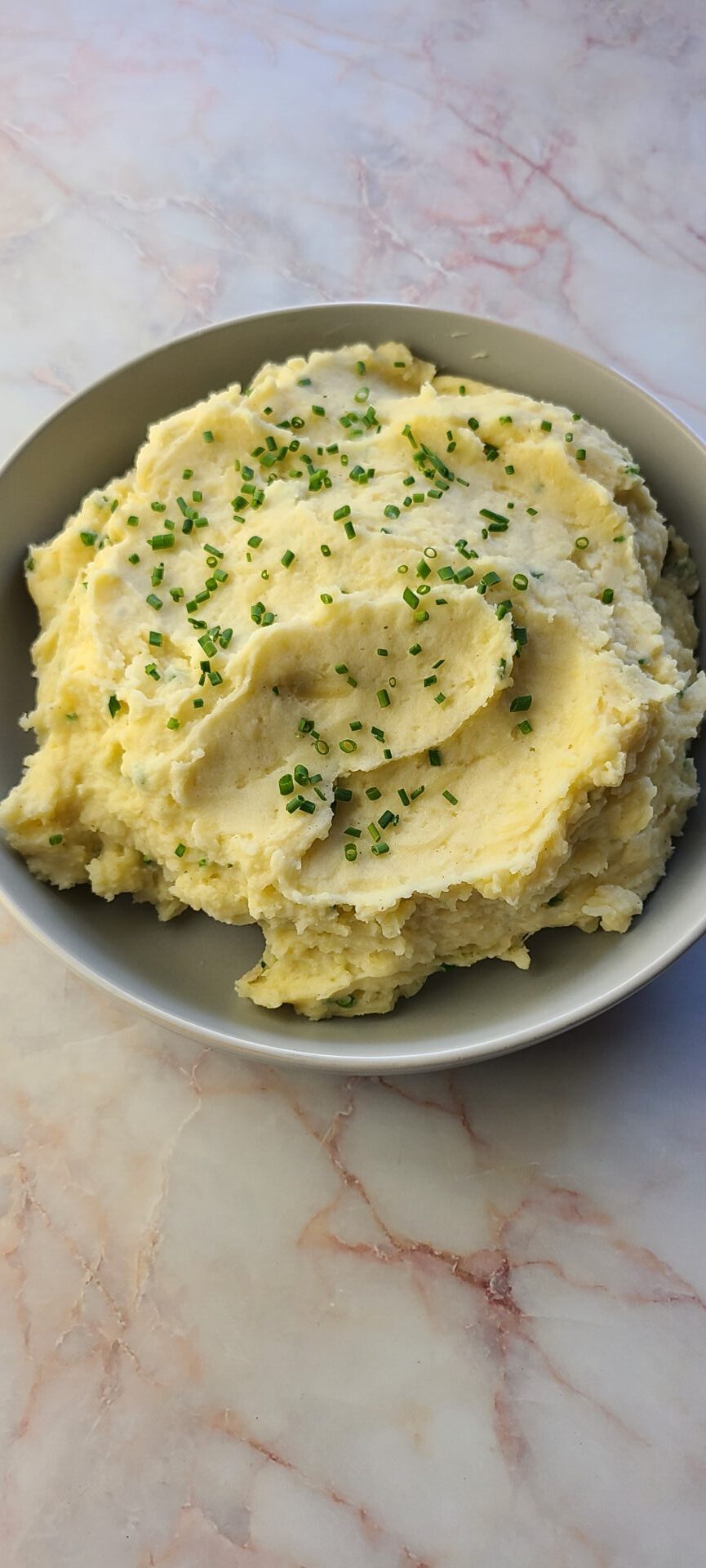 a bowl of creamy, cheesy mashed potatoes on a marble countertop
