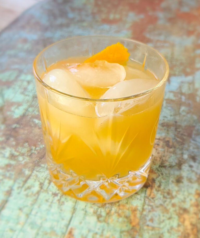 a bourbon cocktail in a crystal glass on an old board